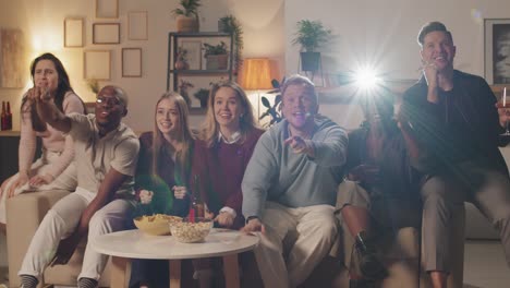 group of friends at a house party, they watch tv while celebrating and hugging