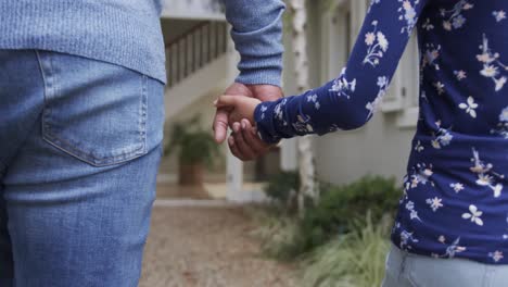 Mid-section-of-biracial-father-and-daughter-holding-hands-in-garden,-slow-motion