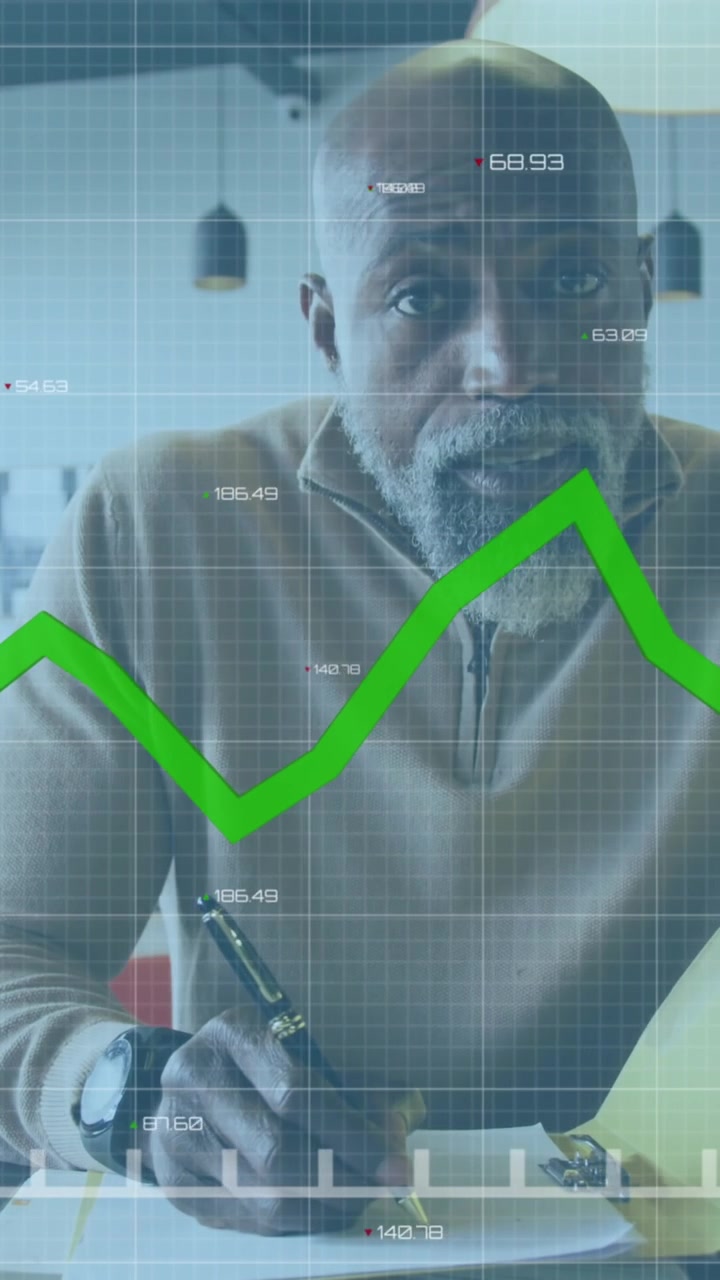 Animation of green graph over african american man taking notes and having a video call at office