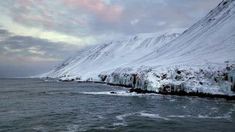 Las-Olas-Ruedan-Contra-Las-Escarpadas-Paredes-Heladas-De-Las-Montañas-En-El-Blanco-Paisaje-Invernal-De-Islandia