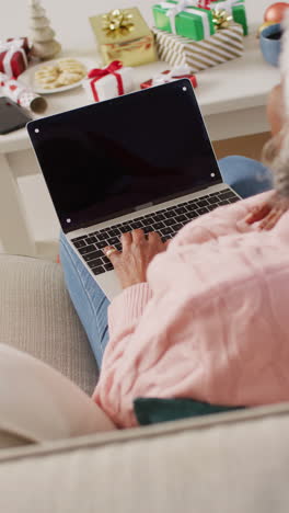 video vertical de una mujer afroamericana mayor haciendo una llamada de video usando una computadora portátil en navidad