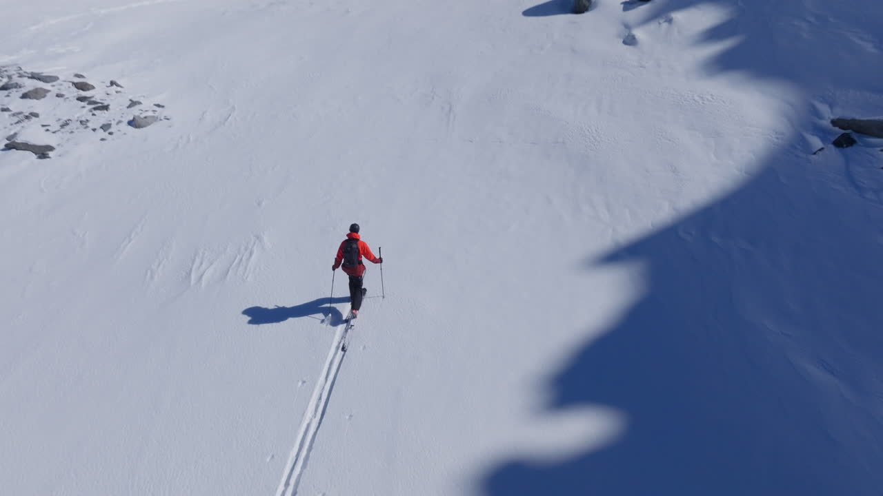 Ripresa aerea con drone di scialpinisti che salgono attraverso neve fresca incontaminata nelle Alpi svizzere. Paesaggio invernale incontaminato, avventura fuoripista, luce soffusa del mattino e atmosfera alpina cinematografica
