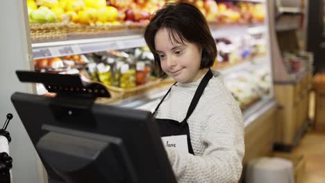 Trabajador-Con-Síndrome-De-Down-Usando-Una-Tableta-Digital-En-La-Sección-De-Productos-Frescos-De-Una-Tienda-De-Comestibles