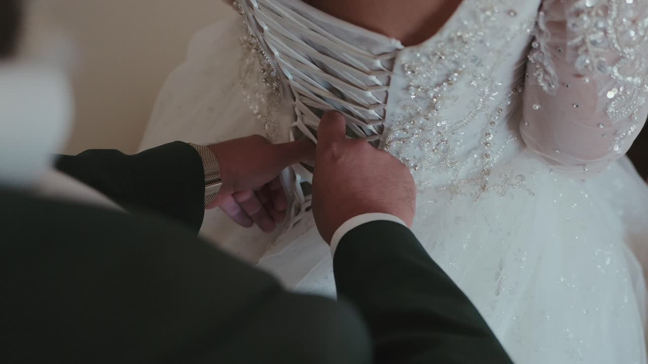 Close view of groom tying corset on bride wedding dress