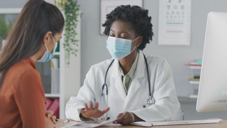 médico o consultor femenino con máscara se reúne con una paciente femenina para discutir las exploraciones