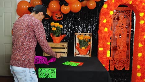 latino man placing perforated papel picado on día de muertos altar