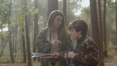 mujer caucásica y su hijo caminando en un parque natural mientras exploran la naturaleza y navegan con brújula y mapa