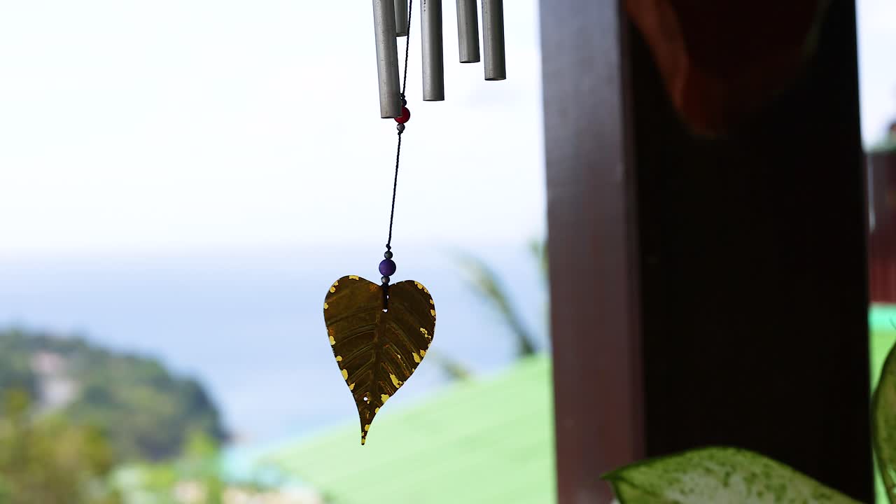 A wind chime with a leaf pendant sways gently in a coastal breeze, set against a tranquil seaside backdrop