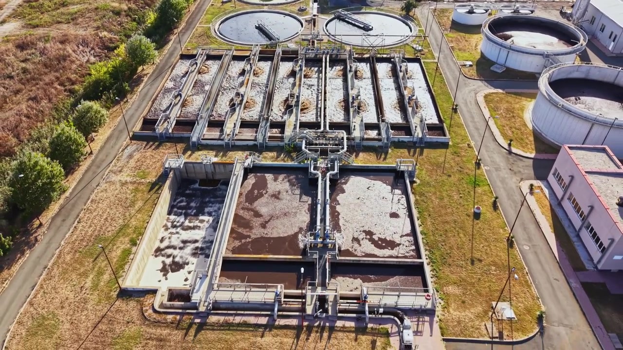 Impianto di trattamento delle acque situato in un'area industriale che mostra vari serbatoi e unità di processo sotto la luce solare intensa.