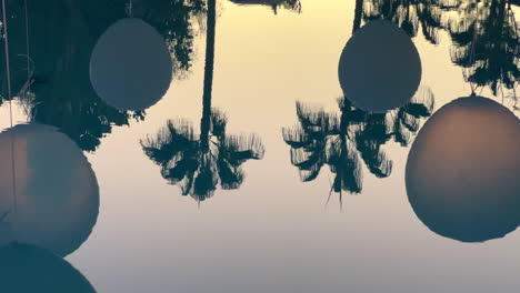 reflejo del agua de la piscina de una fiesta en un lugar tropical con globos blancos y palmeras, tiro de 4k