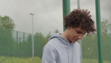 young smiling active male basket player in gray sweatshirt holding ball while standing on playground