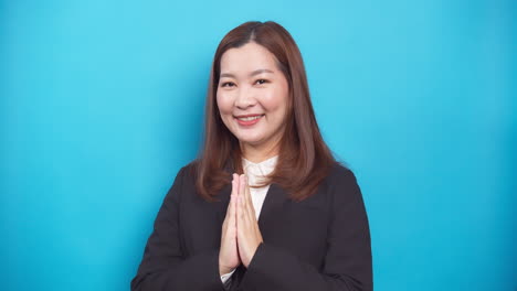 Beautiful-Thai-businesswoman-in-a-black-suit-guests-Sawadee-with-a-smile-on-blue-background