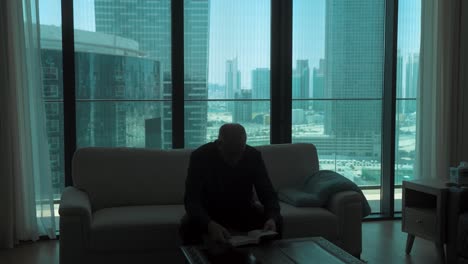 elderly man reading a book in a modern apartment with a city view