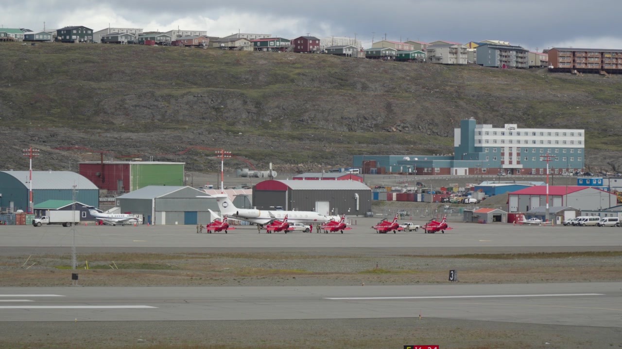Toma con teleobjetivo que muestra una fila de icónicos aviones a reacción rápidos BAE Hawk de los Red Arrows de la RAF, de color rojo brillante, aparcados uno junto al otro en la plataforma del aeropuerto de Iqaluit