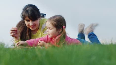 Mama-Genießt-Zusammen-Mit-Einer-Lustigen-Tochter-Die-Natur,-Liegt-Auf-Dem-Grünen-Gras-Und-Studiert-Die-Umliegende-Landschaft