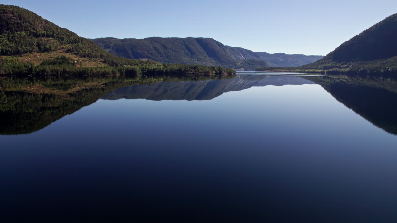 Slow aerial pan over Byglandsfjord in Norway on a clear day, Tree covered mountains reflect in the still water