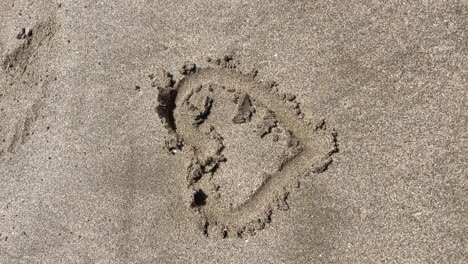 tracking shot of a heart drawn in the wet sand of the beach