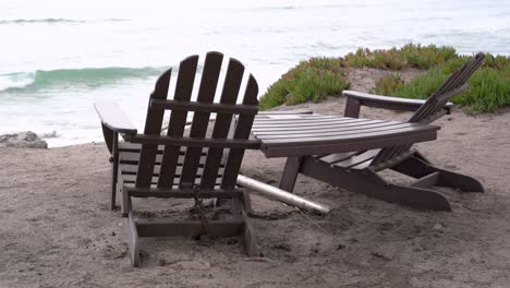 dos sillas de madera y una mesa junto a la playa