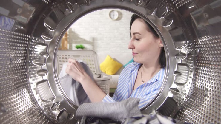 Giovane donna che tira fuori il bucato pulito dalla lavatrice, vista dall'interno