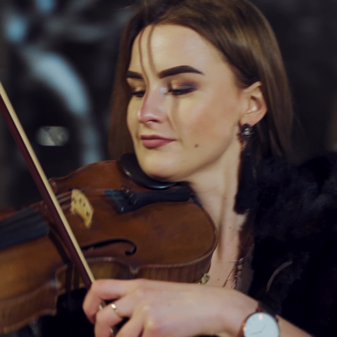 A charming girl is playing the violin in a black coat in the evening in the street. Camera motion around