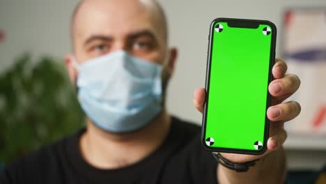 man wearing medical mask showing phone with chroma green screen, vaccination passport with qr code, international coronavirus covid 19 vaccine certificate on mobile device, green zone.