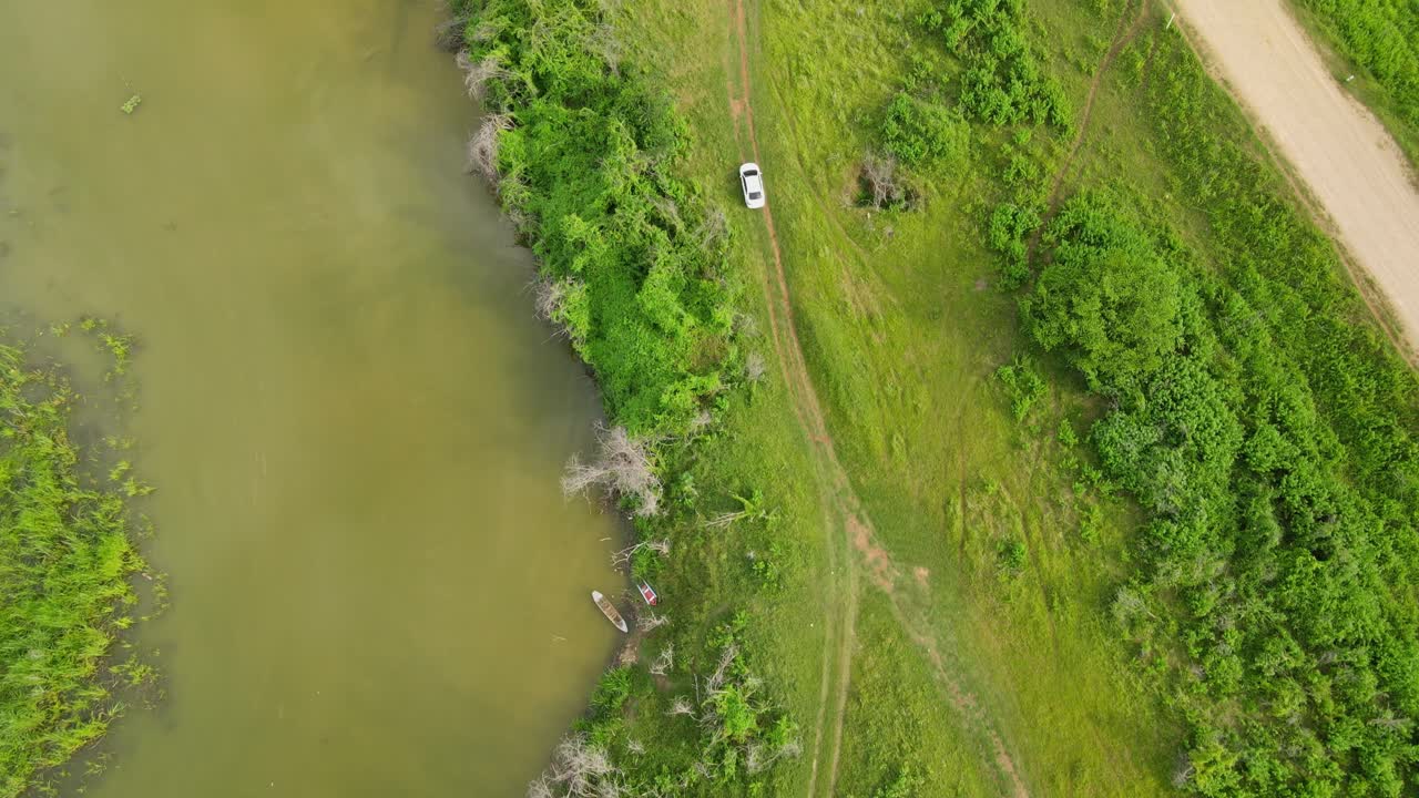 un automóvil que se mueve por un camino de tierra que va a la carretera principal al lado del río, captura aérea, muak klek, saraburi, tailandia