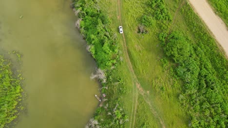 a car moving on a dirt road going to the main road next to the river, aerial capture, muak klek, saraburi, thailand