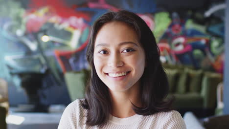 young asian woman smiling to camera in front of mural, head and shoulders, close up