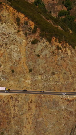 stunning mountains with little greenery growing on. road in the middle of rocks at the edge of cliff. sunny day footage from air. vertical video
