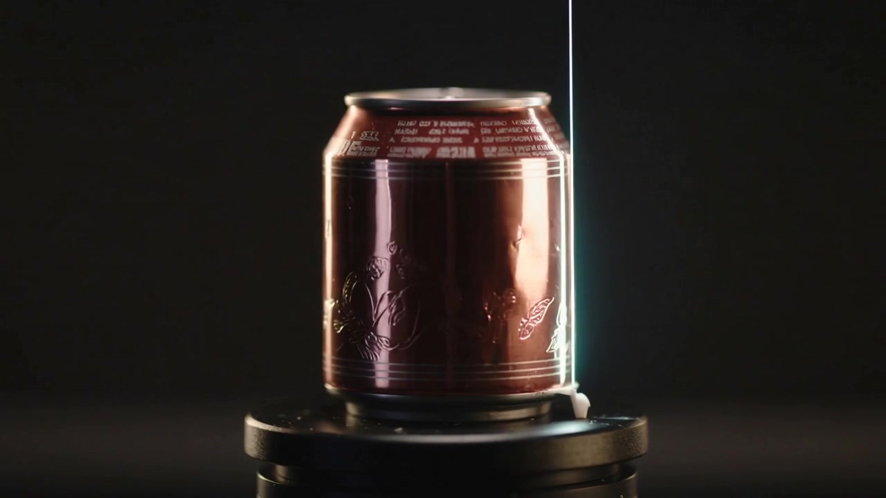 Una striscia di luce verticale che appare e scorre su una lattina di metallo posta su un piedistallo nero, rivelando la goffratura e il bordo.