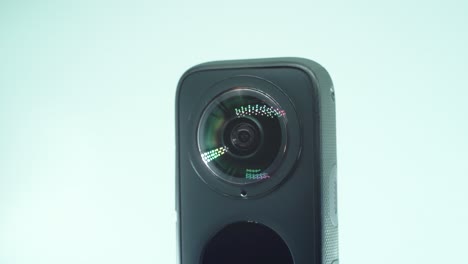 a close up shot of a 360 camera with dual lens, two lens covers, shiny studio lighting reflecting, round screen, on a rotating stand, slow motion, 4k video