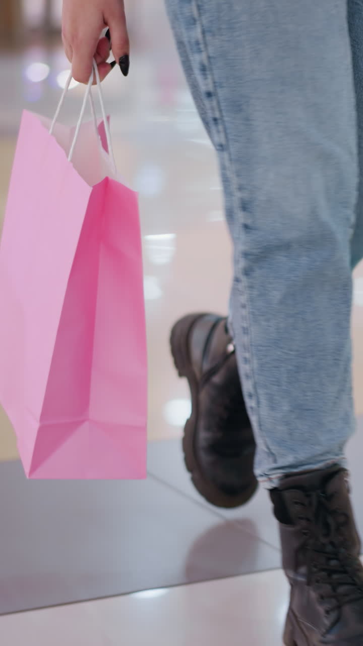 검은색 부츠와 청바지를 입은 사람이 손에 쇼핑백을 들고 현대적인 쇼핑몰을 자신 있게 고 있는 모습, 흐릿한 배경으로 바닥에 매끄러운 타일