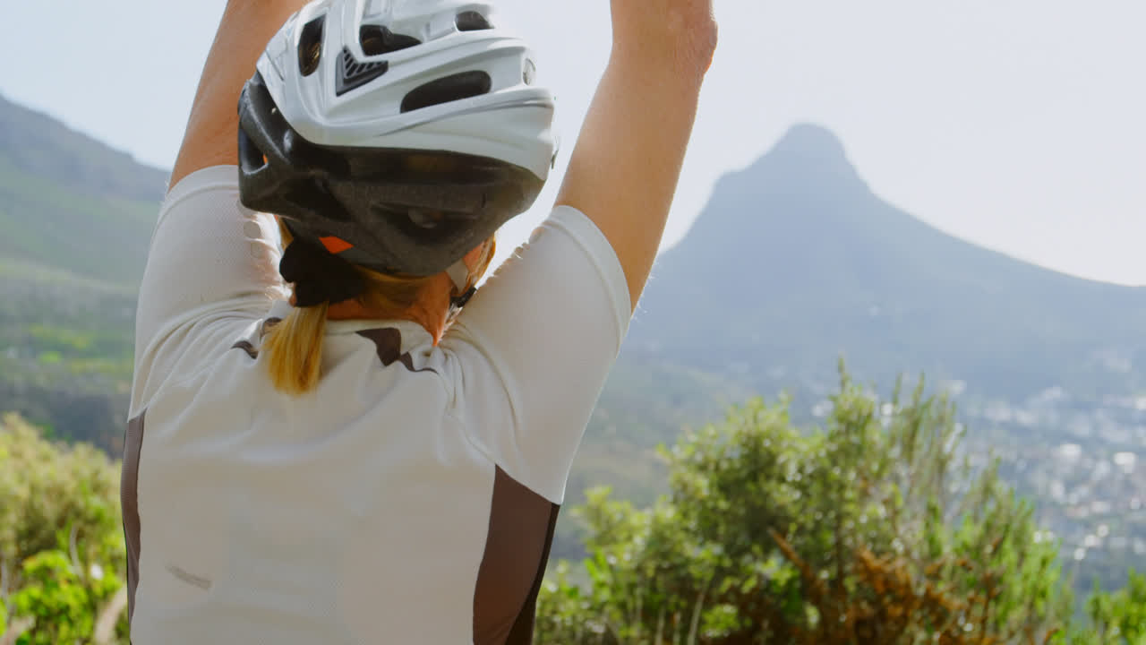 ciclista sénior de pie con los brazos en alto en el campo 4k