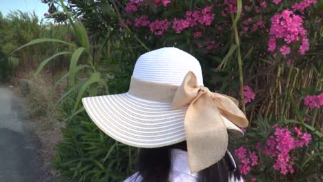 following back of female in summery hiking outfir walking next to flowers in greek countryside