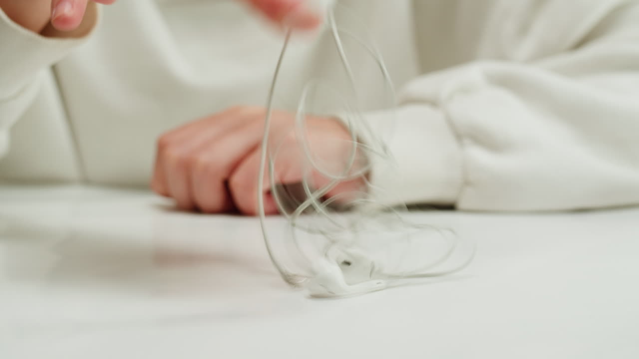 Tangled wires on table close-up. Trying to untangle many messy cables.Young woman trying to untangle the white headphones.