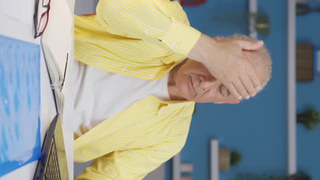 Vertical-video-of-Home-office-worker-old-man-see-his-failure-on-laptop.