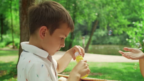 mujer divirtiéndose con su hijo en el parque. niño alegre soplando burbujas de jabón al aire libre