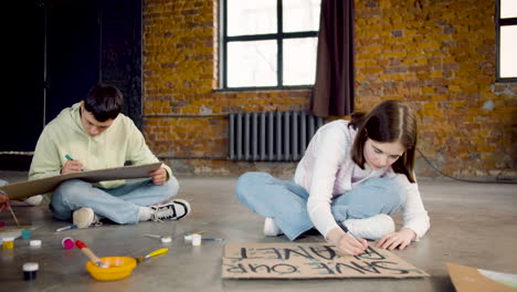 zoom out of young environmental activists painting placards sitting on the floor