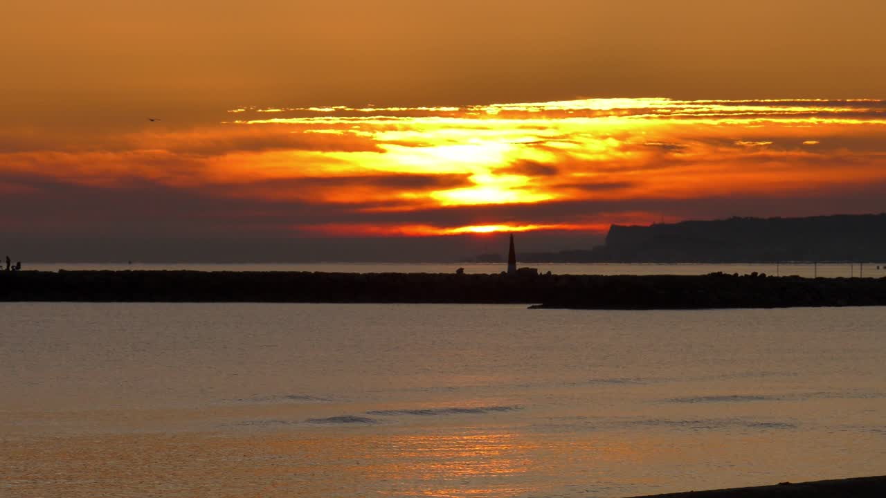 Golden sunrise over calm sea with harbor wall silhouette