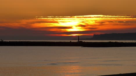 golden sunrise over calm sea with harbor wall silhouette