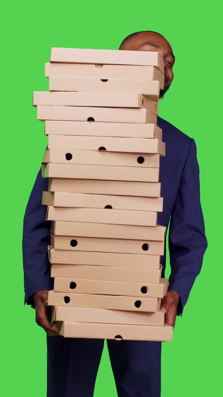 Vertical video: Front view of african american manager carrying big pile of pizza boxes
