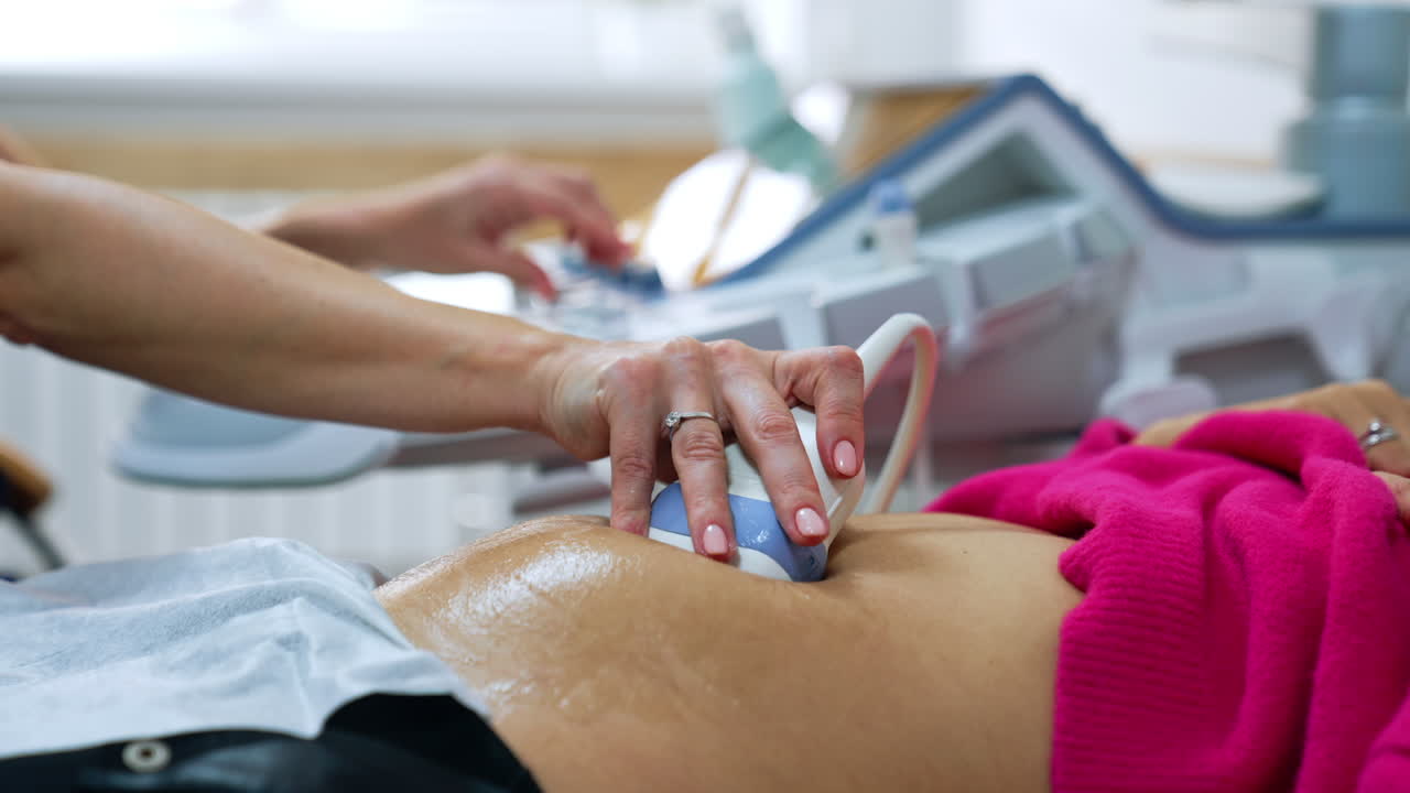 Bare female hand holds the ultrasonic device on woman's belly. Pregnancy scanning at hospital. Close up.