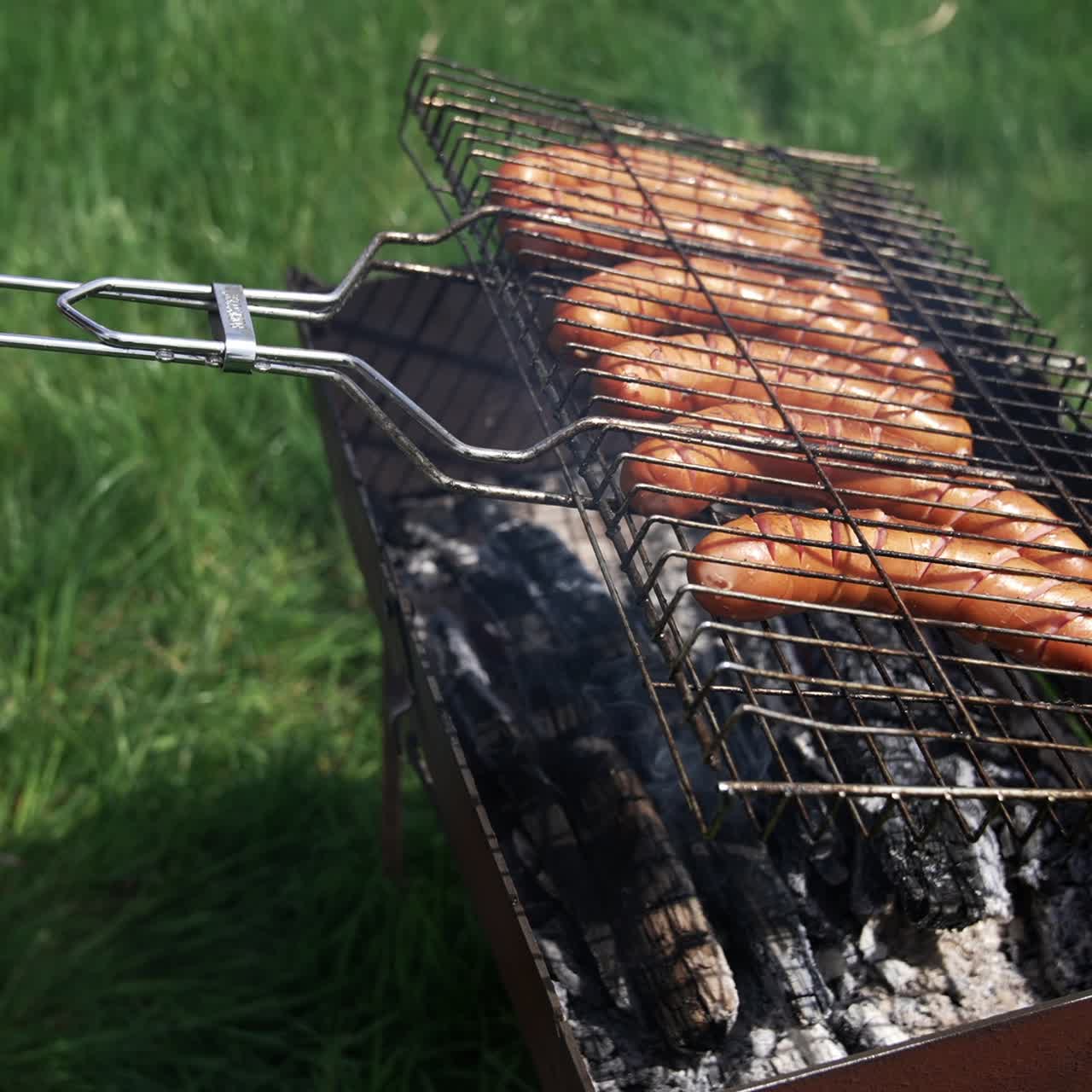 Barbecue grill. Cooking sausages for picnic. Hot dog sausages being cooked and turned over on an outdoor grill. Making a picnic