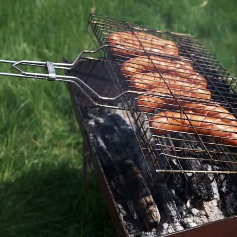 barbecue grill. cooking sausages for picnic. hot dog sausages being cooked and turned over on an outdoor grill. making a picnic