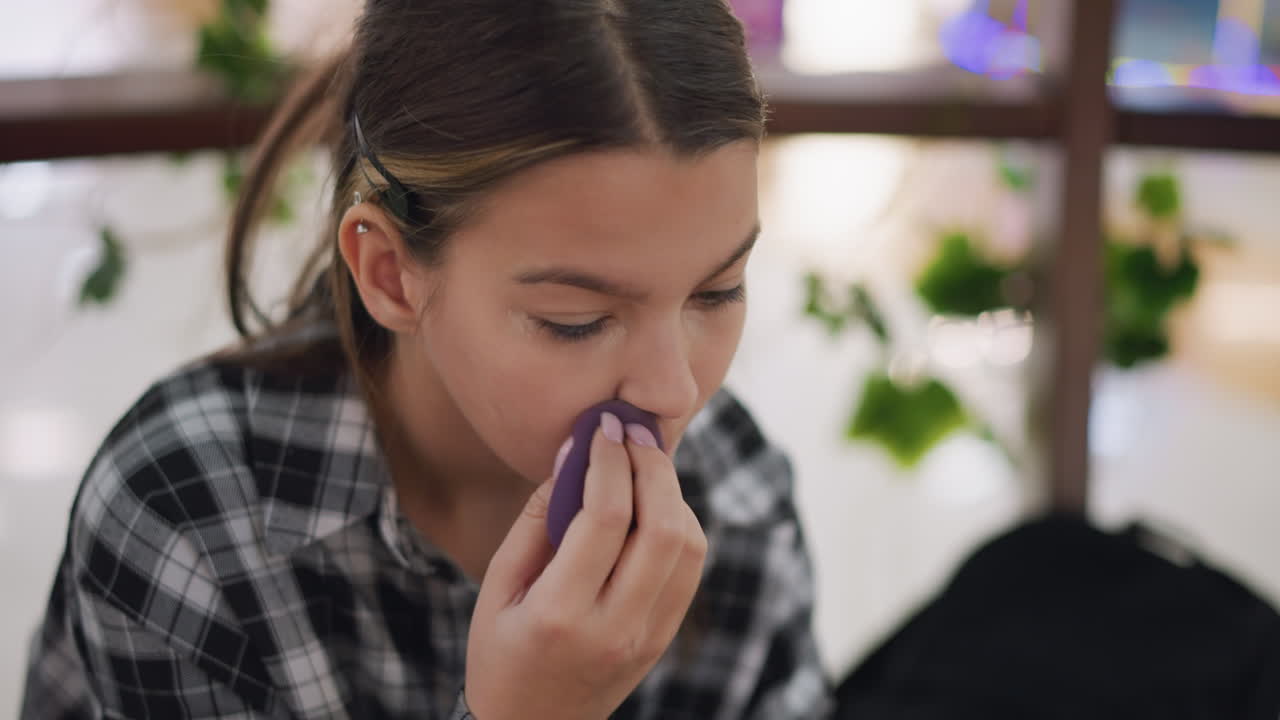 dama enfocada mezclando cuidadosamente el maquillaje al lado de la nariz usando esponja de belleza para un acabado suave, mejorando los contornos faciales con la aplicación precisa de la fundación, iluminación suave destacando el proceso de belleza