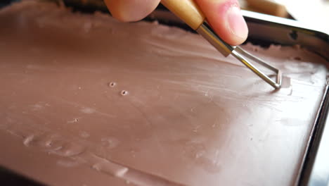 an artist and sculptor carving off brown modeling clay from a large block with a hand tool in a satisfying shaving to begin sculpting his art project in a studio