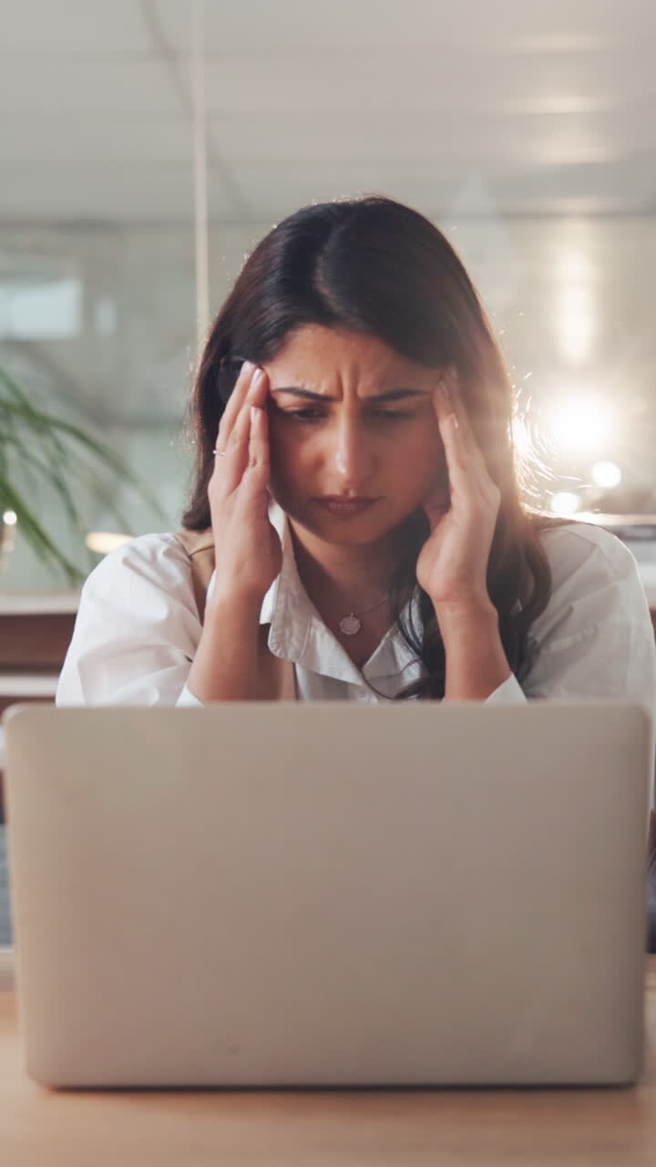 Stressed Young Businesswoman with Headache Overwhelmed by Flying Papers in Office