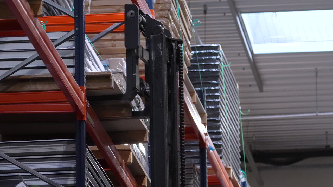 Primo piano del montante di un carrello elevatore che solleva pesanti pallet di legno da scaffalature metalliche in una fabbrica di lavorazione del legno o in un centro di distribuzione.