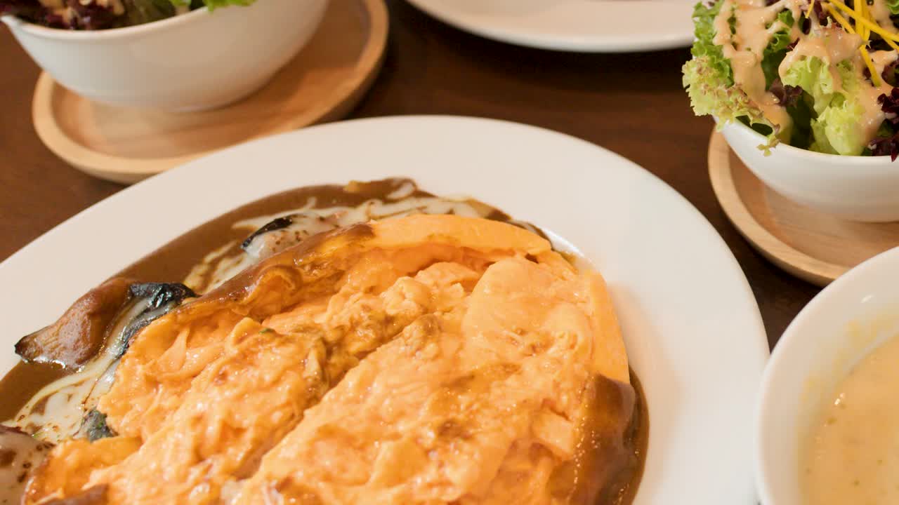 Close-up pan of Japanese omelette rice, salad, soup, and bread in warm restaurant lighting