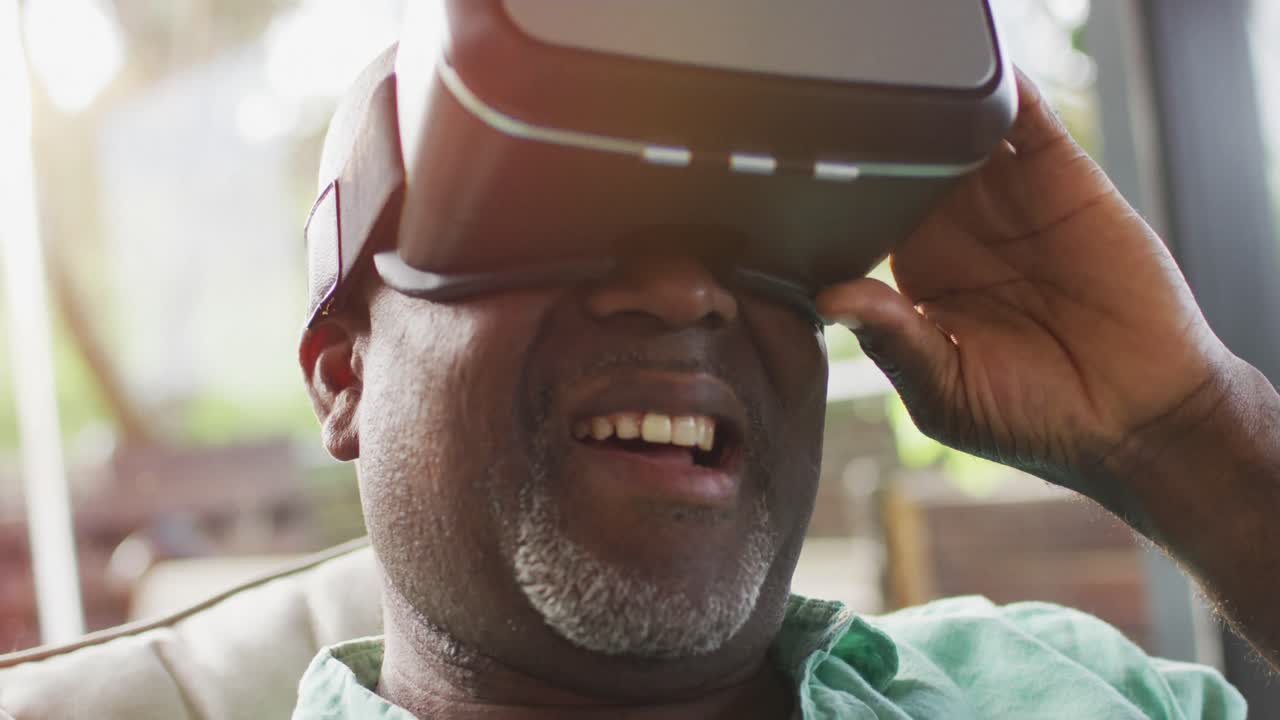 행복한 아프리카계 미국인 노인 남자가 vr 헤드 ⁇ 을 사용하고 웃으며  ⁇ 은 거실에 앉아 있습니다.